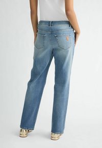 Svetlo modri široki jeans z klasičnim petim žepnim dizajnom, ki vključuje šivano logo na zadnjem žepu in gladko teksturo denima.