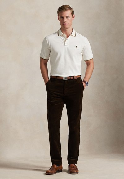 Bílá polokošile s hnědým lemováním, doplněná tmavě hnědými manšestráky a hnědými koženými botami. Má klasický střih a decentní logo.