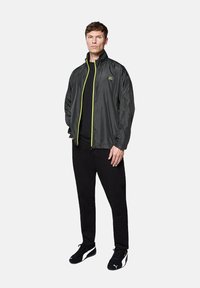 Lekka, szara kurtka z wysokim kołnierzem i neonowo-żółtym zamkiem. Noszona na czarną koszulę, w zestawieniu z czarnymi spodniami i czarnymi sneakersami.