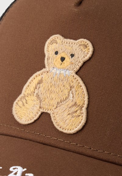 Κεντημένο πατζάκι αρκουδάκι σε μπεζ και καφέ αποχρώσεις σε καφέ υφασμάτινη επιφάνεια, με λεπτομέρειες μαύρα μάτια και μύτη.