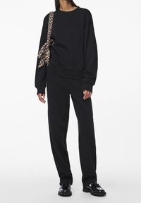 Černý svetr a odpovídající kalhoty z jemné tkaniny. Svetr má kulatý výstřih, dlouhé rukávy a pásek s leopardím vzorem uvázaný v pase.