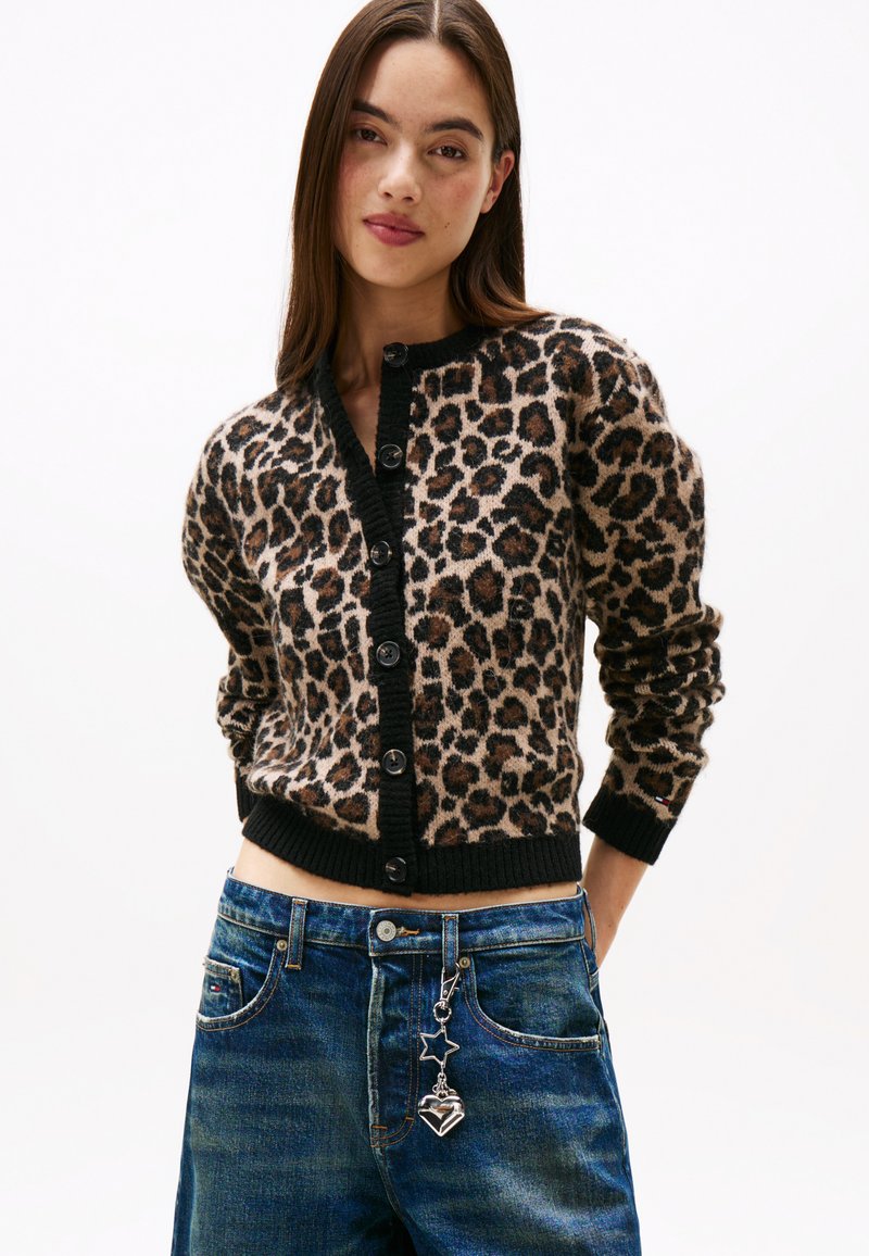 Kardigan med leopardmønster og svarte kanter, med en rad av svarte knapper og ribbede mansjetter, brukt over middels vaskede denimjeans.