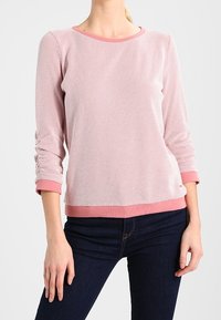 Suéter de textura rosa claro con un escote redondo y mangas tres cuartos, con un dobladillo y puños de color rosa en contraste. Combinado con jeans oscuros.