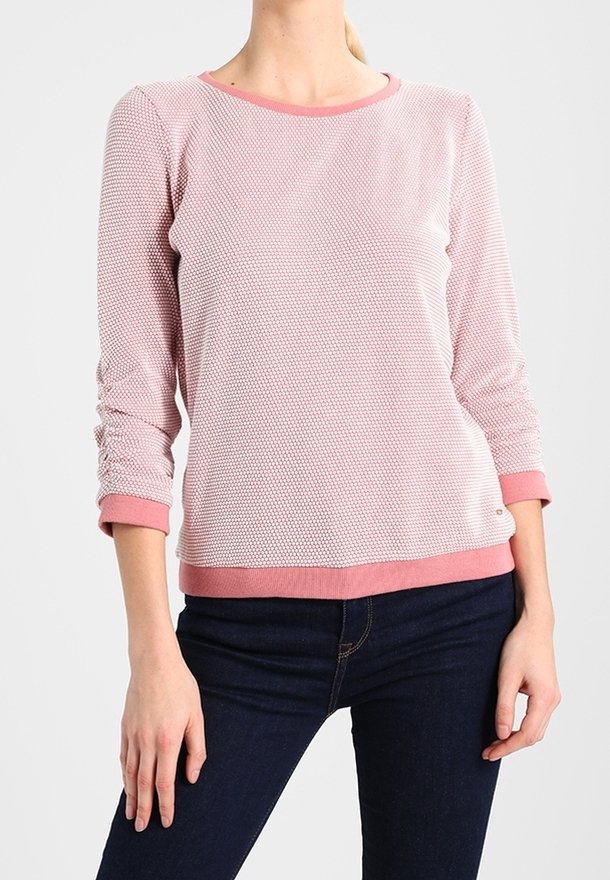 Suéter de textura rosa claro con un escote redondo y mangas tres cuartos, con un dobladillo y puños de color rosa en contraste. Combinado con jeans oscuros.