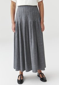 Gonna maxi plissettata grigia in un tessuto testurizzato, con una vita aderente e una silhouette ampia e fluida. Abbinata a scarpe nere con cinturino a T.