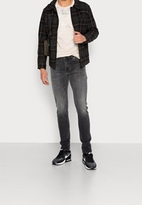 Camisa a cuadros en negro y gris sobre una camiseta gris clara, combinada con jeans ajustados en gris oscuro y zapatillas negras con acentos blancos.