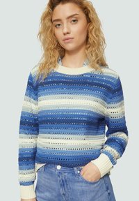 Blau-weißer gestreifter Pullover mit offenem Strickmuster, geripptem Ausschnitt und Bündchen sowie einem lässigen cropped Schnitt. Getragen über heller Denim.