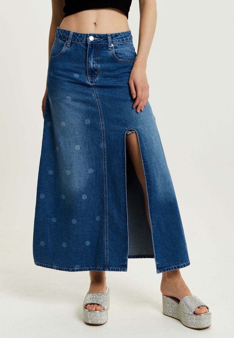 Denim maxi skirt in dark blue with a front slit, polka dot pattern, and classic five-pocket design. Paired with silver platform sandals.