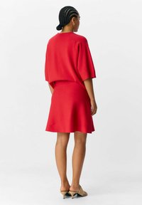 Abito rosso con una vestibilità rilassata, maniche corte e orlo svasato. Tessuto liscio senza motivi visibili. Abbinato a sandali con tacco beige.