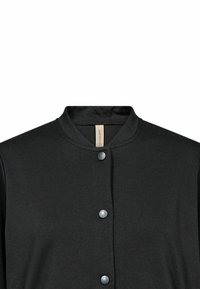 Giacca nera con bottoni a pressione e un colletto rotondo, dotata di quattro bottoni a finitura opaca visibili sul davanti.