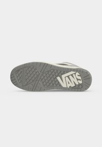 Подметка на сива маратонка Vans, показваща вълнова шарка и голямо лого на Vans отдолу на обикновен светъл фон.