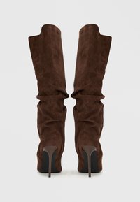 Καφέ μπότες έως το γόνατο από σουέντ με χαλαρή σχεδίαση, μυτερό μπροστινό μέρος και ψηλό τακούνι στιλέτο. Ομαλή υφή και διπλωμένο άνω τμήμα.