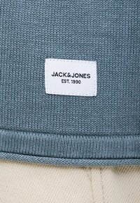 Gros plan sur un tissu tricoté bleu avec un patch rectangulaire blanc affichant le texte "JACK & JONES EST. 1990".