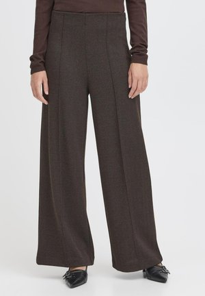 Pantaloni a gambi larghi in houndstooth marrone con vita alta, caratterizzati da cuciture verticali e un tessuto testurizzato. Indossati con scarpe nere a punta.