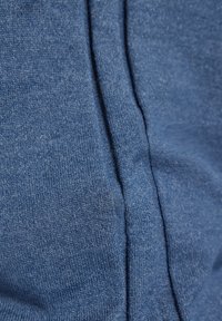 Blauer Strickstoff mit einer glatten Textur und einem Nahtdetail. Das Material wirkt weich und leicht, geeignet für lässige Kleidung.