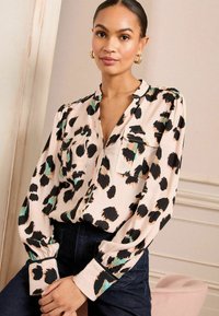 Svijetlo ružičasta bluzica s apstraktnim leopard mrljama u crnoj i zelenoj boji, dugme sprijeda, džep na prsima i duge rukave s detaljima na manžetama.