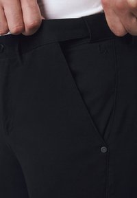 Czarne dopasowane spodnie z teksturowanej tkaniny, o wąskim kroju, z dekoracyjnym detalem w postaci guzika i ukośnymi kieszeniami bocznymi.