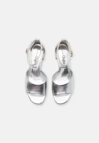 Sølv høyhælte sandaler med en glatt metallisk finish, bred frontreim, ankelreim og blokkhelt. Innvendig har de en blank tekstur.
