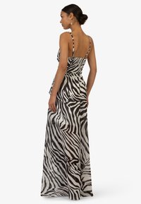 Maxi-Kleid mit einem schwarz-weißen Zebra-Print, dünnen Spaghettiträgern und einem fließenden, leichten Stoff, der elegant fällt.