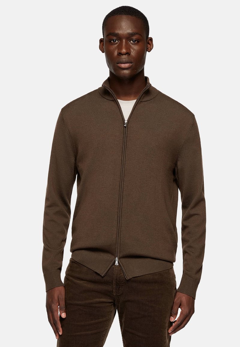 Brown zip-up sweater in ribbed texture, featuring a high collar and fitted style, paired with dark brown corduroy pants.