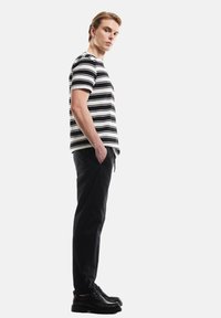 Zwart-wit gestreepte T-shirt met korte mouwen, gedragen met zwarte broeken en zwarte schoenen. Het shirt heeft een relaxte pasvorm en een ronde hals.