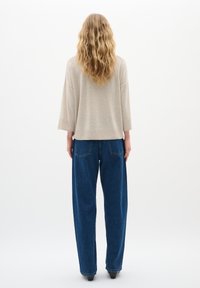 Beige, laza fazonú pulcsi, háromnegyedes ujjakkal, magas derekú, egyenes szárú sötétkék farmernadrággal párosítva.