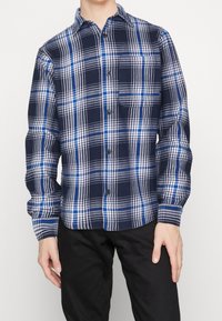 Camicia a maniche lunghe a quadri blu e navy con colletto button-down, dotata di una tasca sul petto e chiusura con bottoni. Tessuto morbido.