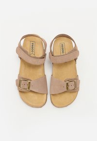 Bruna mockaskor med platt sula, två justerbara remmar, en spänneaccent och en mjuk beige innersula. Logotyp synlig på innersulan.