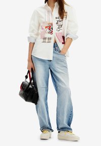 White button-up shirt with graphic patchwork, featuring colorful Mickey Mouse design and plaid accents. Paired with light blue baggy jeans and sneakers.