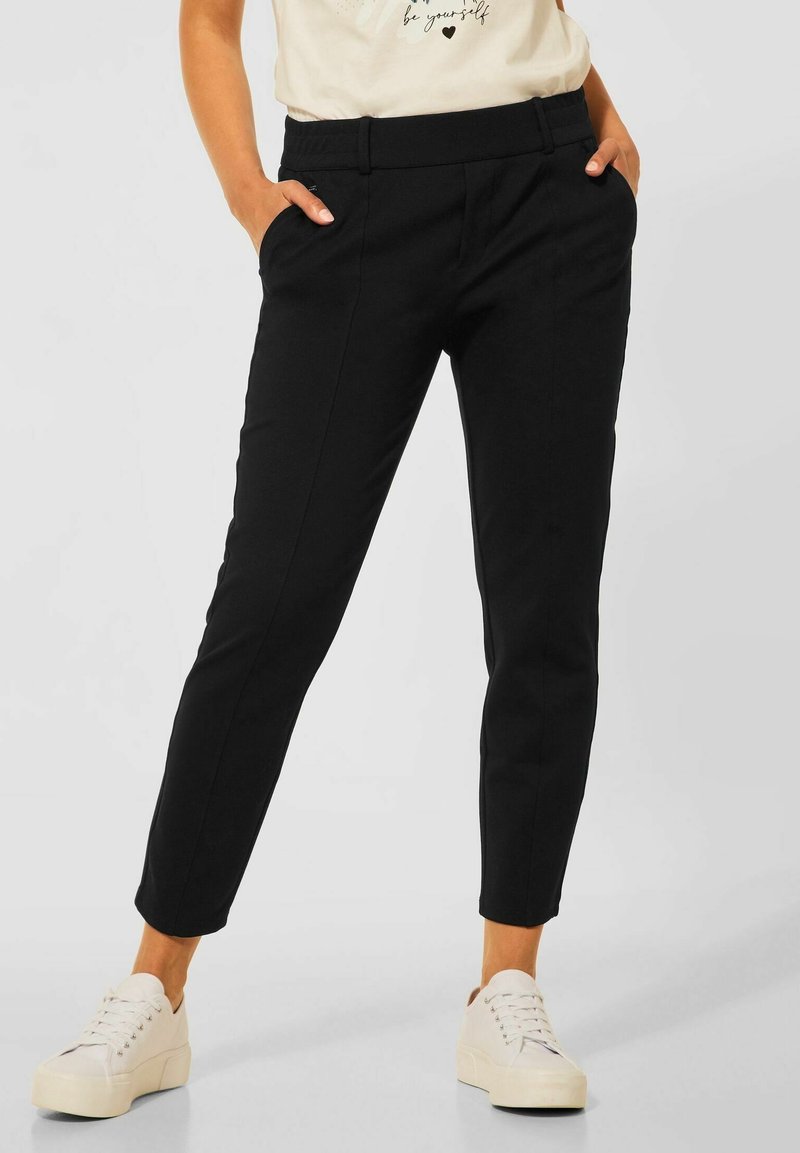 Černé tapered kalhoty s dvěma postranními kapsami, elastickým pasem a hladkým povrchem. Nosit s bílými platformovými teniskami.