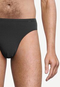 Zwarte bikini slipjes met een geometrisch hexagonaal patroon, gemaakt van rekbare stof, hebben een low-rise ontwerp en een gladde tailleband.