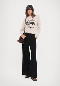 Beige knitted sweater with black dachshund graphic and text, paired with high-waisted black wide-leg trousers and brown heeled ankle boots.
