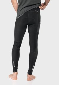 Schwarze Sportleggings mit einer glatten Textur, ausgestattet mit verstärkten Einsätzen, reflektierenden Akzenten und Reißverschlüssen an den Knöcheln für verbesserte Beweglichkeit.