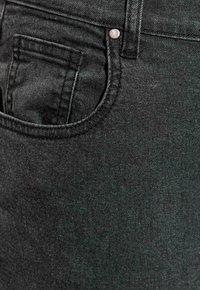 Czarna tkanina dżinsowa o gładkiej fakturze, z przednią kieszenią i metalowym guzikiem jako akcent w klasycznym fasonie spodni dżinsowych.