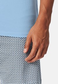 Himmelblaues T-Shirt mit kurzen Ärmeln, kombiniert mit gemusterten Shorts, die ein navyblaues und weißes Karodesign aufweisen. Eine sichtbare Hand ruht auf den Shorts.