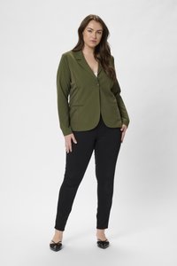 Blazer vert olive avec une fermeture à un bouton et deux poches latérales, associé à un pantalon skinny noir et des ballerines noires à bout pointu.