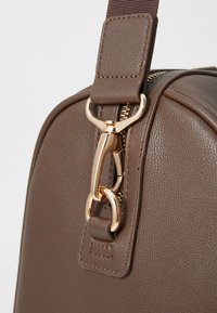 Brown leather handbag with a textured finish, featuring a gold-tone zipper and hardware, and a robust adjustable strap.