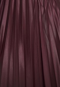 Burgundy red, redős szövet, sima, selyemhez hasonló textúrával, amelyen függőleges, egyenletesen elhelyezkedő redők és fényes bevonat látható.