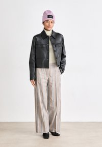Giacca nera in pelle cropped con chiusura a bottoni, dolcevita beige, pantaloni a righe a gamba larga e berretto in maglia viola chiaro con logo.