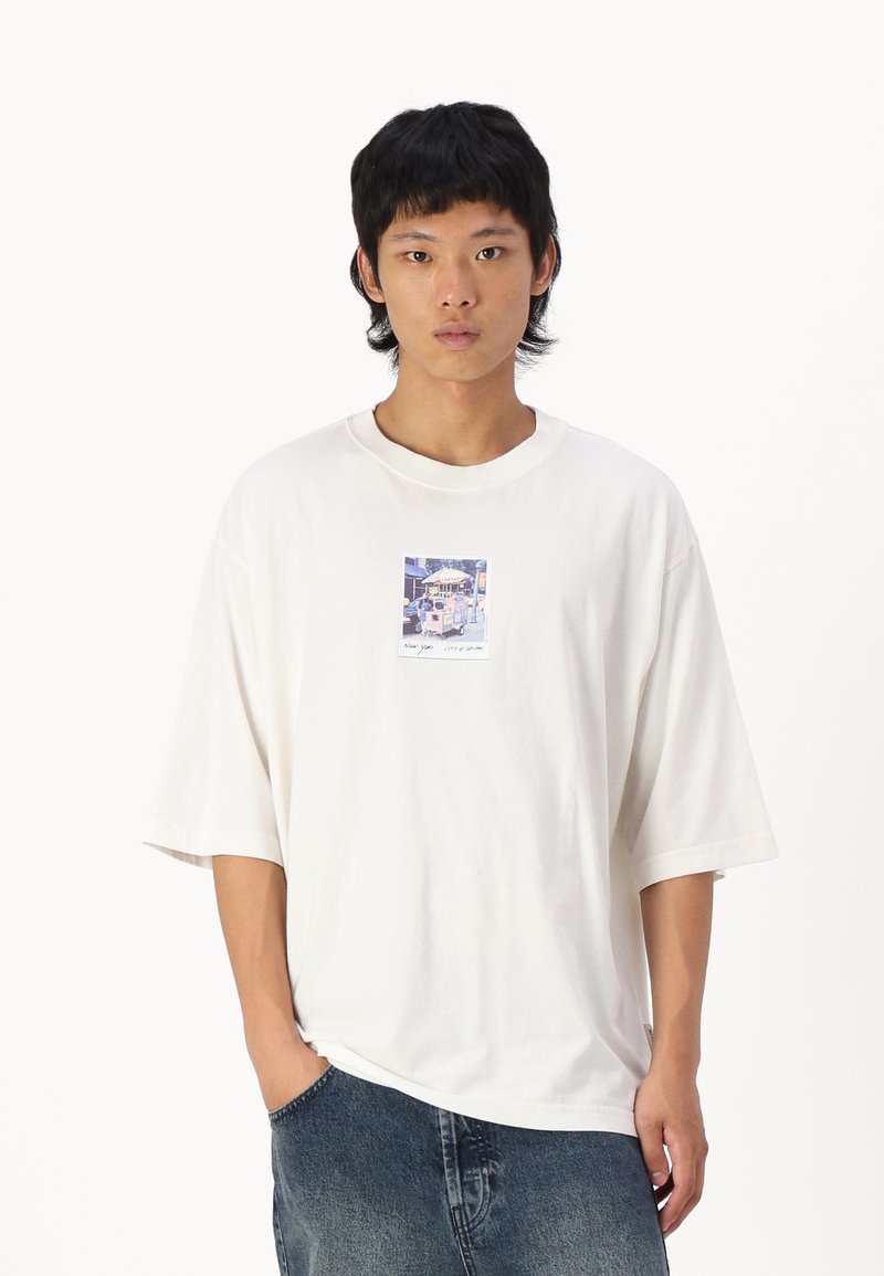 Hvid oversized t-shirt lavet af bomuld. Har et firkantet grafisk print centreret på brystet. Casual, boxy pasform med korte ærmer og rund hals.