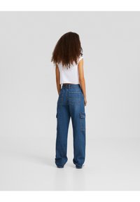 Pantalones cargo de denim de tiro alto en azul, con bolsillos frontales y laterales, cintura elástica y un corte amplio; combinados con una camiseta básica blanca corta.