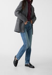 Grå överdimensionerad kavaj, vinröd högkrage topp, ljusblå raka jeans och svarta loafers med samlad textur. Vit bakgrund.