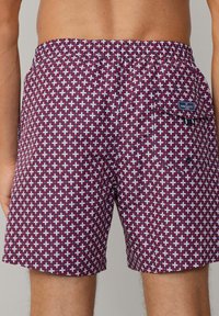 Bordeauxfarbene Schwimmhosen mit einem geometrischen Muster in Weiß und Hellblau. Mit elastischem Bund und einer seitlichen Tasche mit einem Logo-Patch.