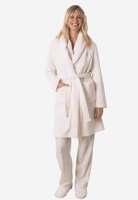 Bílý, měkký župan s šálovým límcem a páskem v pase, se dvěma bočními kapsami. Nošený přes bílé kárované kalhoty a sladěné pantofle.