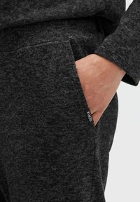 Dunkelgrauer Pullover aus weichem, strukturiertem Stoff mit einer Taschenverzierung. Verfügt über einen kleinen weißen Aufnäher mit dem "sockx"-Logo.