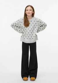 Grauer Strickpullover mit Pünktchen, weiten Ärmeln und geripptem Saum, kombiniert mit schwarzen weit geschnittenen Hosen und beigen Knöchelstiefeln.