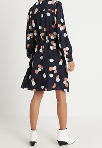 Granatowa sukienka o luźnym kroju, z wielokolorowymi kropkami w odcieniach bieli, różu i czerni. Elastyczny pas, długie rękawy i detale w postaci guzików.