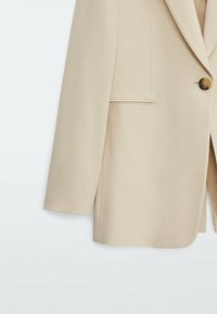 Vaalean beige bleiseri, jossa on jäsennelty muotoilu, pitkät hihat, yksittäinen napitus ja huomaamaton sivutasku. Silkkinen, hyvin leikattu kangas.