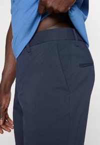 Σκούρα μπλε παντελόνια με υφή υφάσματος, με πλαϊνές τσέπες και καλοραμμένη εφαρμογή. Η μέση έχει ελαστική και διακριτική σχεδίαση.