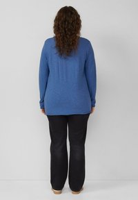 Blauwe lange mouwen shirt van zacht materiaal, gecombineerd met zwarte wijde broek. Zichtbare stiksels op de zoom en mouwen van het shirt.